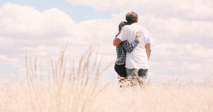A photo of a couple hugging eachother out in a field looking out towards the horizon